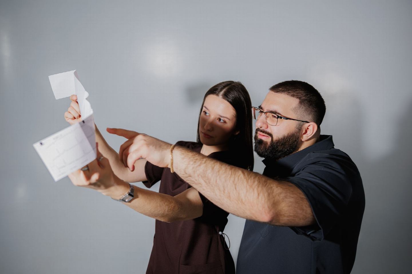 Zwei Erwachsene halten ein Blatt Papier hoch und deuten gemeinsam auf eine Stelle darauf.